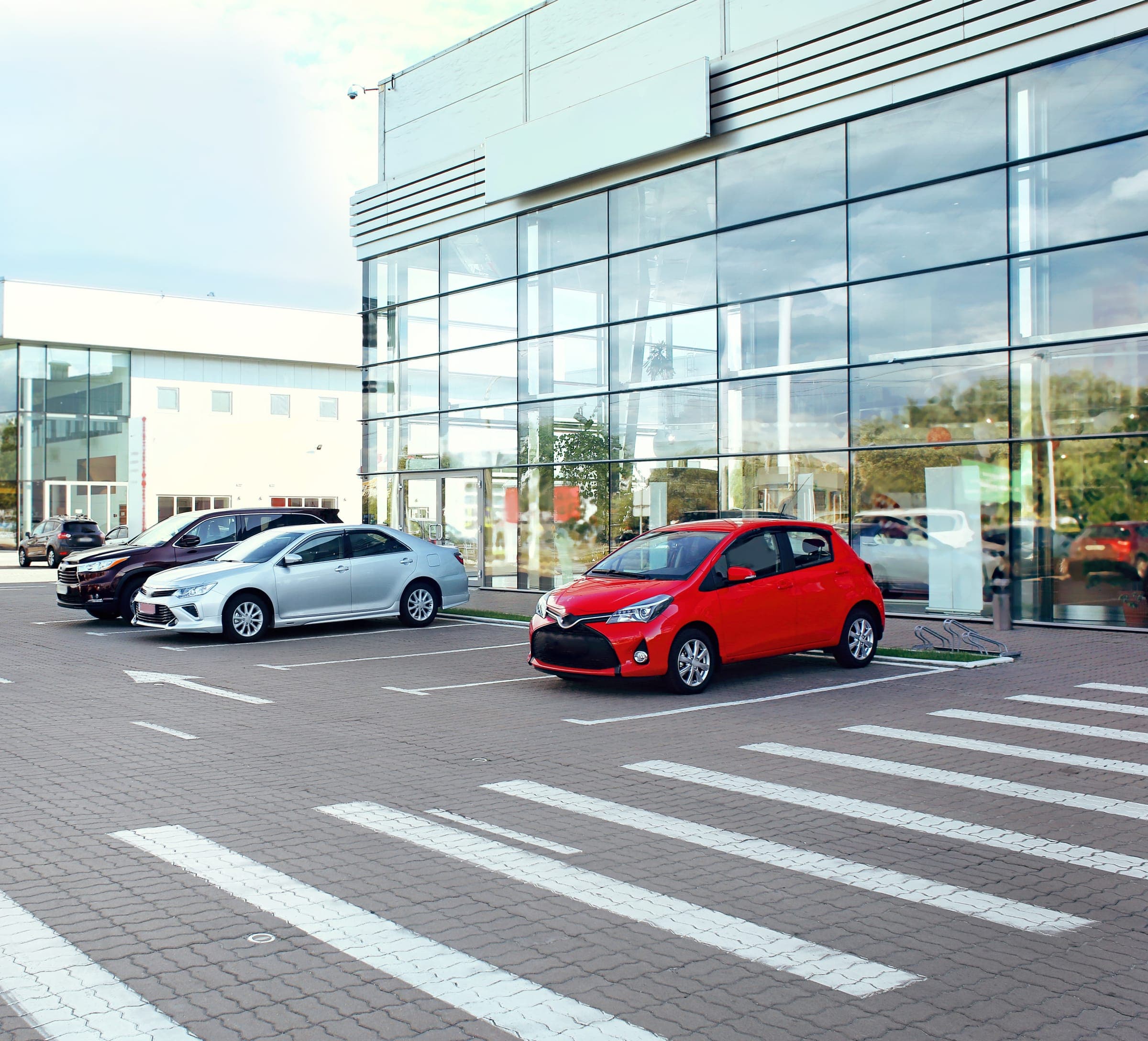 Autohaus mit Glasfront, davor gepflasterte Ausstellungsfläche mit Fahrzeugen